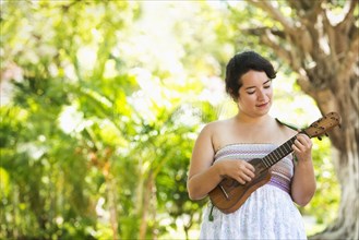 Hispanic musician playing ukulele in park