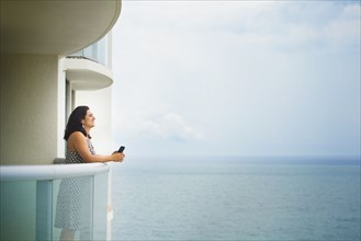 Hispanic woman admiring ocean from hotel balcony