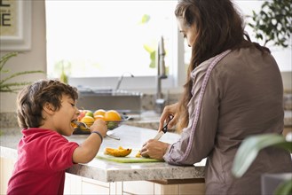 Hispanic mother and son eating fruit in kitchen