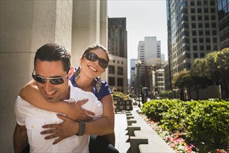 Hispanic man carrying girlfriend piggyback in city
