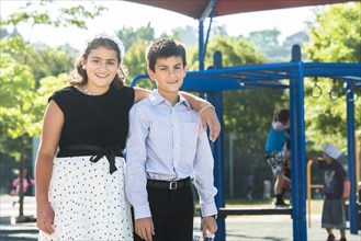 Proud well-dressed Mixed Race brother and sister posing on playground