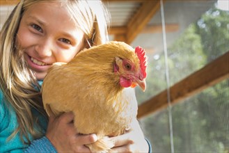 Caucasian girl hugging chicken in chicken coop
