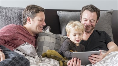 Caucasian fathers using digital tablet on bed with son