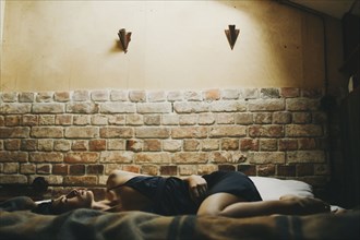 Caucasian woman laying on bed near brick wall