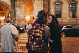 Caucasian woman kissing man on cheek in city at night