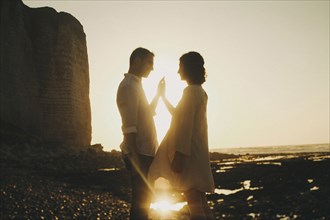 Caucasian couple pressing hands on beach at sunset