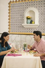 Smiling Hispanic couple eating salad and laughing in restaurant
