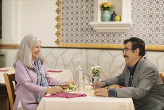 Smiling older couple eating salad and laughing in restaurant