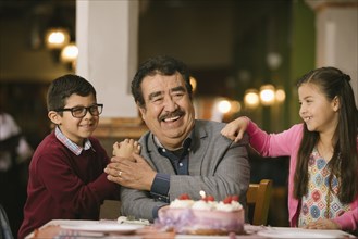 Hispanic grandchildren celebrating birthday of grandfather in restaurant