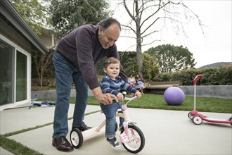 Grandfather pushing grandson on tricycle
