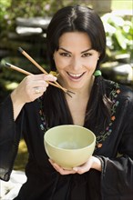 Hispanic woman eating from bowl with chopsticks