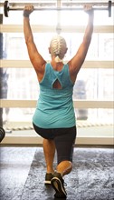Older woman lifting barbell in gymnasium