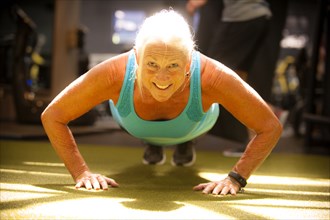 Smiling older woman doing push-up on gymnasium floor