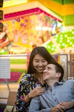 Smiling couple cuddling on bench in amusement park