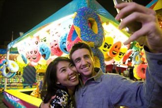 Smiling couple posing for cell phone selfie in amusement park