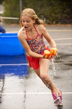 Caucasian girl running with dripping sponge in parking lot