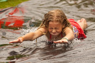 Caucasian girl sliding in water on outdoor plastic tarp