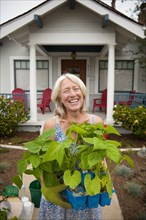 Portrait of smiling Caucasian woman holding tray of plants near house
