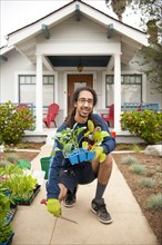 Portrait of smiling Black man holding tray of plants near house