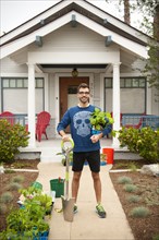 Portrait of smiling Hispanic man holding shovel and plants near house