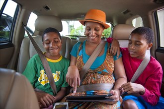 Black mother and twin sons using digital tablet in car