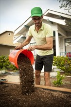 Hispanic man pouring bucket of dirt in raised garden