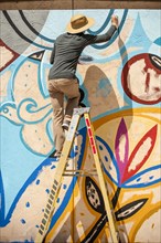 Man standing on ladder painting mural on wall
