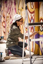 Woman kneeling on tarp painting mural on wall