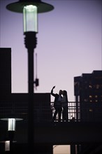 Couple standing on balcony posing for cell phone selfie at night