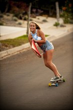 Caucasian girl skateboarding on hill carrying surfboard