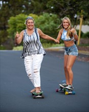 Caucasian mother and daughter holding hands while skateboarding