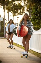Teenage girls carrying surfboards on skateboards