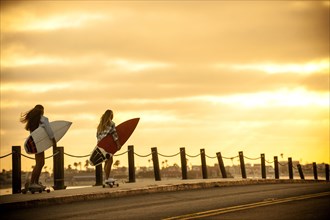 Teenage girls carrying surfboards on skateboards