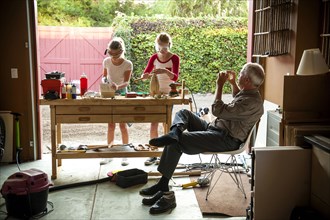 Grandfather photographing granddaughters building birdhouse in garage