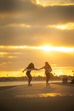 Girl holding hands while skateboarding on waterfront at sunset