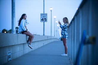 Teenage girl photographing friend sitting on wall