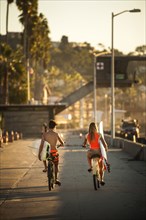 Teenage boy and girl riding bicycles carrying surfboards