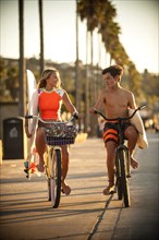 Teenage boy and girl riding bicycles carrying surfboards