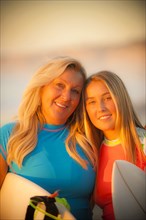 Portrait of smiling Caucasian mother and daughter holding surfboards