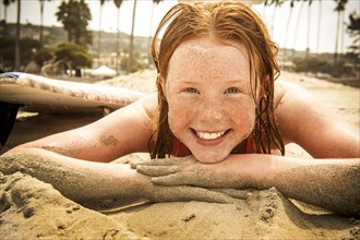 Portrait of smiling girl laying on beach covered with sand