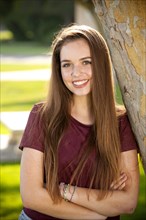 Portrait of smiling Caucasian teenage girl leaning on tree