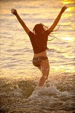 Teenage girl running into ocean at sunset