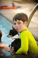 Caucasian boy in swimming pool holding dog