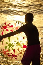Silhouette of Caucasian boy holding beach ball at sunset