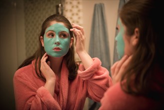 Caucasian girl applying facial mask in mirror