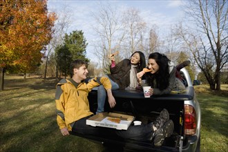 Friends eating pizza in back of truck