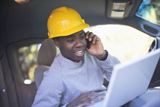 Black man wearing hard hat in vehicle using laptop