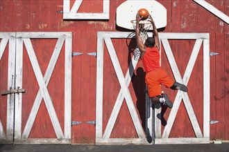 Black man dunking basketball outside barn