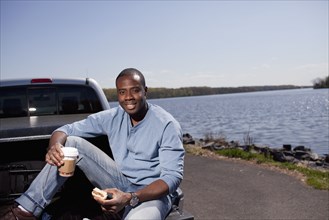 Black man sitting in truck bed eating lunch