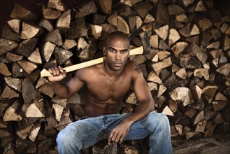 Bare chested African American man near woodpile holding ax